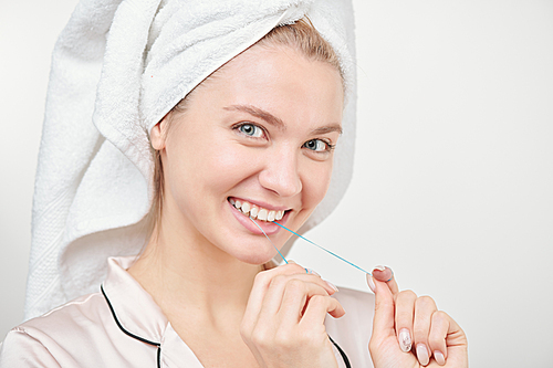 Cheerful healthy young woman with toothy smile using dental floss in front of camera in isolation