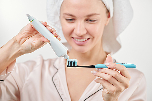 Hand of healthy young woman applying toothpaste on toothbrush during morning hygiene procedures