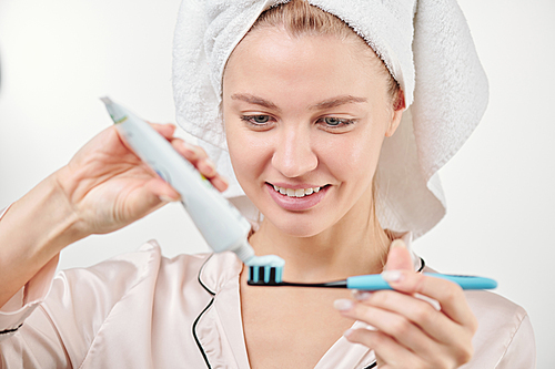 Healthy young smiling woman applying toothpaste on toothbrush before brushing teeth in the morning