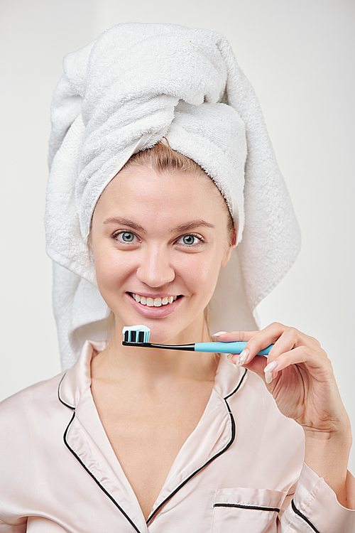 Pretty young healthy woman with toothy smile holding toothbrush while standing in front of camera in isolation