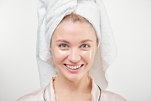 Healthy young woman with toothy smile enjoying refreshening under-eye procedure in isolation