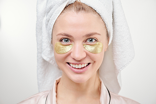 Healthy young smiling woman with revitalising golden under-eye patches standing in front of camera in isolation