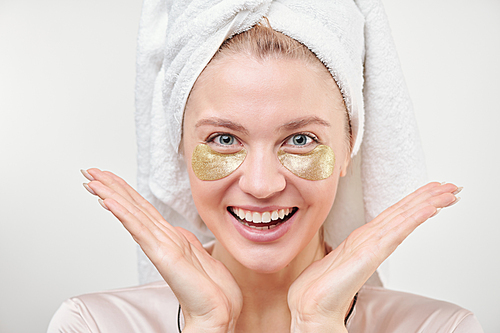 Young excited woman with revitalising golden under-eye patches enjoying skincare procedure in isolation