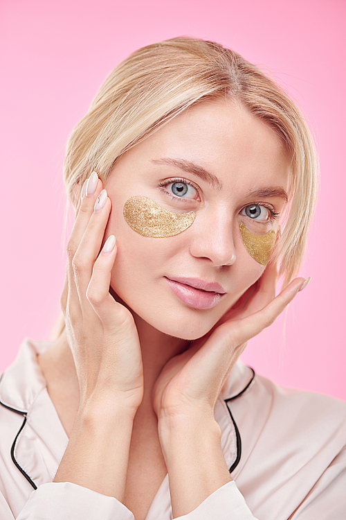 Young beautiful blond woman with golden revitalising under-eye patches taking care of her face