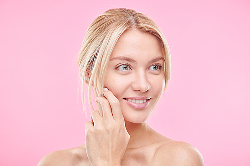 Beautiful young blond woman with clean and radiant face looking with smile in isolation over pink background