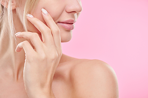 Hand of young healthy woman touching her face while taking care of skin against pink background in isolation
