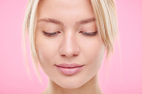 Pretty young blond natural woman looking down in front of camera over pink background