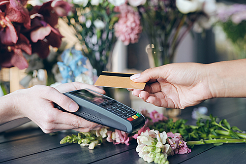 Close-up of customer putting wireless card to terminal while paying for flowers in flower shop, copy space