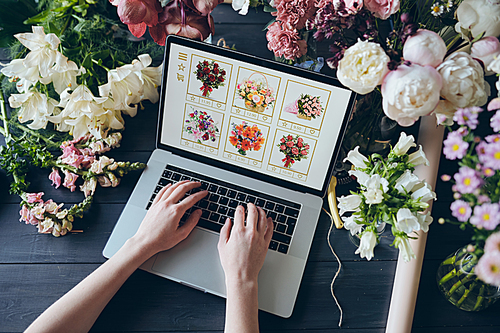 High angle view of unrecognizable woman using laptop while adding flowers to cart on web wholesale store, flower shop concept