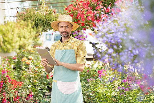 Mature bearded gardener in workwear looking at you while searching for online information about planting