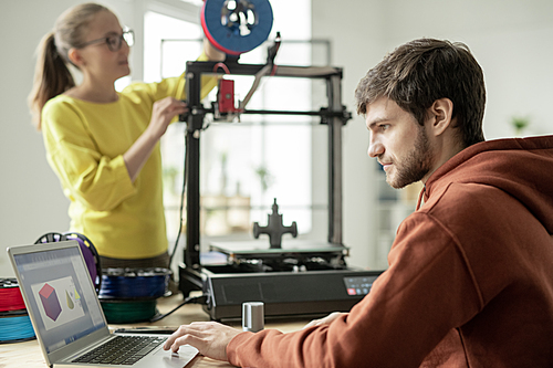 Serious man concentrating on work over new objects on background of his colleague checking spool on 3d printer