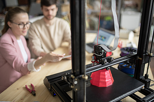 Young manager making presentation of new model of 3d printer while pointing at pink geometric figure being printed