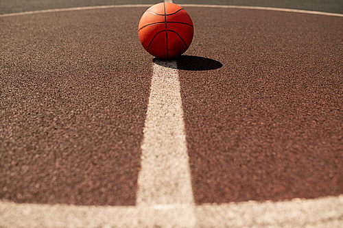 Ball for playing basketball lying in the center of vertical white line on modern stadium or field