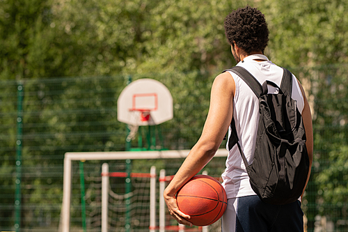 Young basketball player with ball ready for game standing on court or playground on sunny day