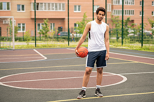 young athlete with ball standing on racetrack of basketball court in front of camera in urban