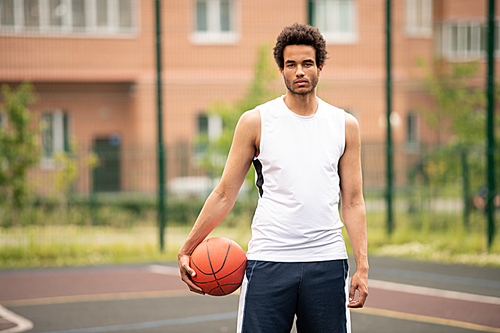 Young handsome basketball player with ball standing on the court on background of architecture