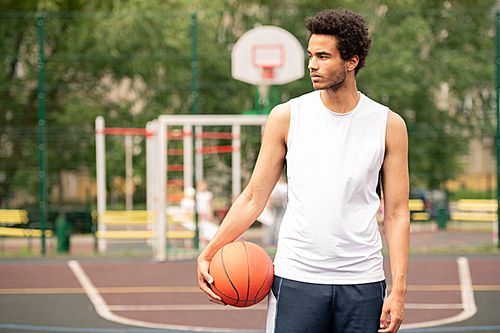 Young sportsman in activewear looking aside while having break between basketball trainings on the court