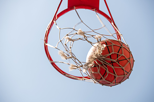 View from below of ball in basketball net with light blue cloudless sky on background