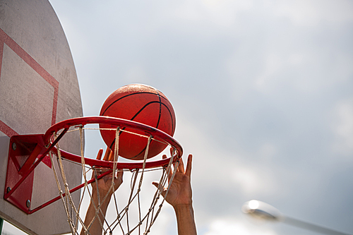 Hands of young basketball player throwing ball into basket during game on outdoor court