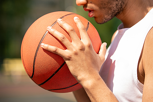Young contemporary male basketball player holding ball by his face and chest while getting ready for pass