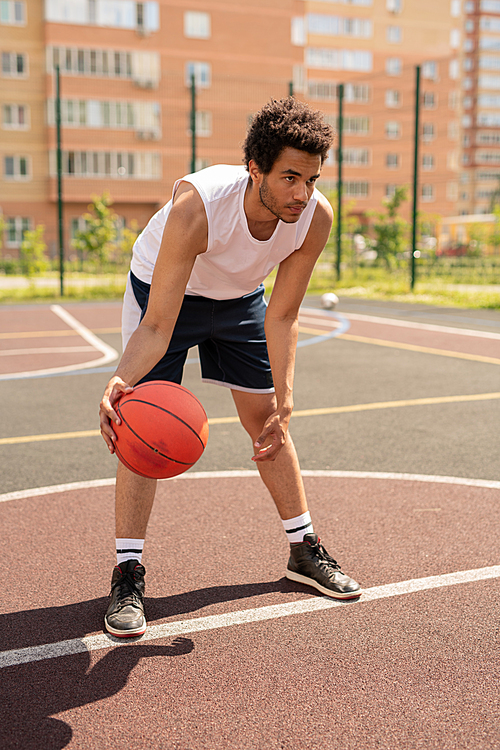 Young basketballer in activewear bending forwards while preparing for throwing ball during play