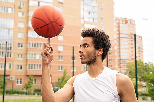 Young active professional basketball player holding rotating ball on forefinger while looking at it