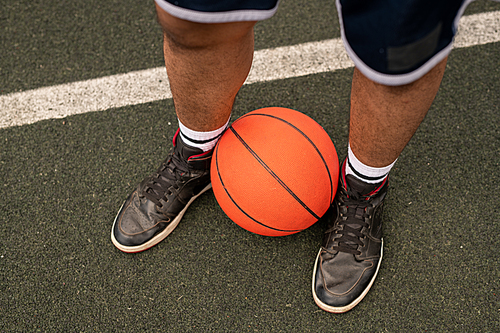 Ball by legs of young professional basketball player standing on playground by white line