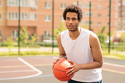Young basketball player with ball looking at basket during game on outdoor court or playground