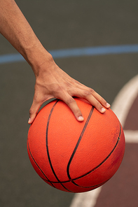 Hand of young active basketballer holding ball while getting ready to throw it during game on the court