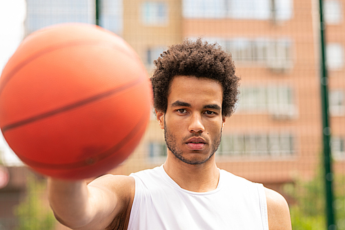 Young serious basketball player looking at you while passing ball or going to throw it in basket