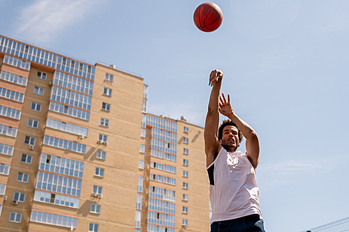 young active basketball player throwing ball while exercising on playground in urban