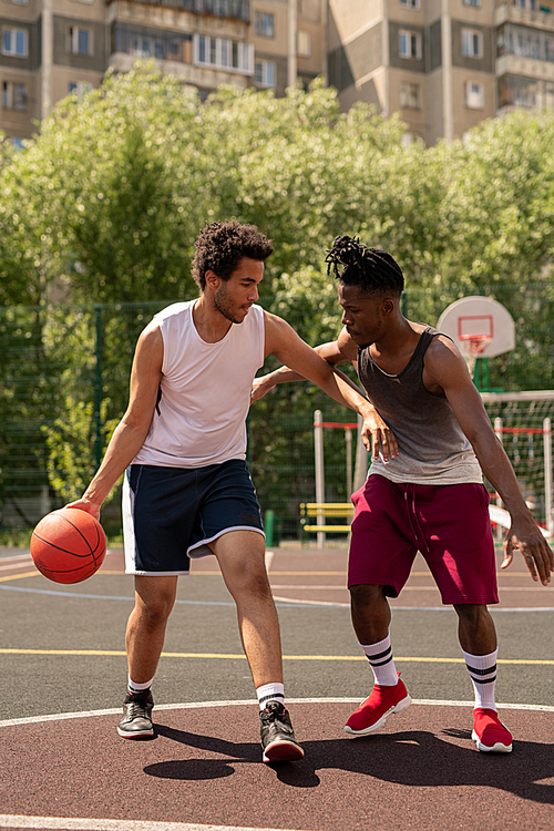 two intercultural basketball playmates playing or training on the court on summer day in urban