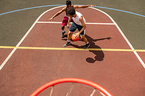 Young basketball player trying to defend the ball from attack of rival during game on outdoor court