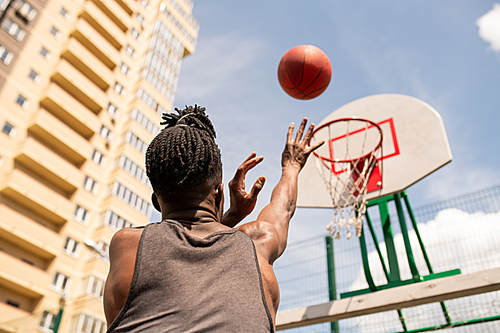 rear view of young african basketball player throwing ball in basket while training in urban