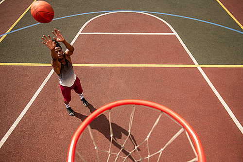 Young professional basketballer in activewear throwing ball in basket while standing on the court