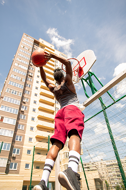 African basketball player jumping while going to throw ball in basket with blue sky above