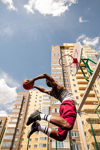 View from below of young African basketballer in jump throwing ball in basket during outdoor training