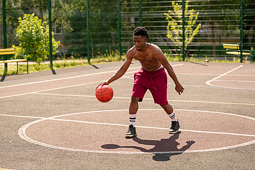 Young shirtles basketball player moving down playground while exercising with ball while training