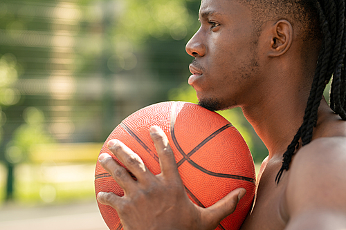 Side view of young multicultural shirtless sportsman holding ball between his chest and chin