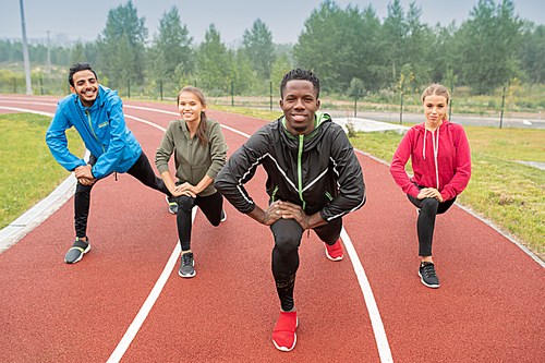 Healthy young intercultural friends in activewear exercising on race tracks of outdoor stadium during workout