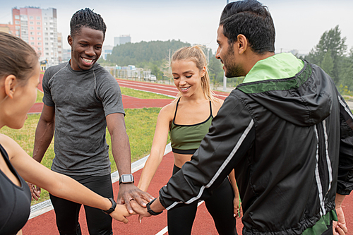 Young successful marathon participants in activewear making circle while keeping their hands on top of each others on stadium