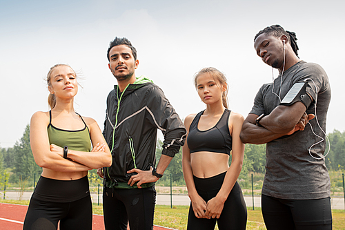 Contemporary young multicultural people in sportswear looking at you while standing on outdoor stadium