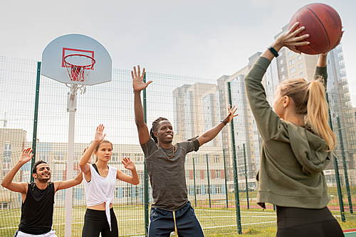 Group of intercultural students or friends in sportswear playing basketball on playground in urban environment