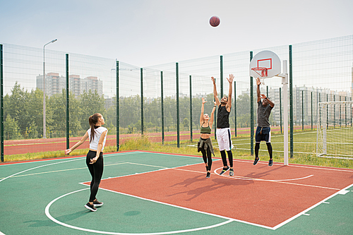 Team of young intercultural friends or students working out on basketball court on summer day