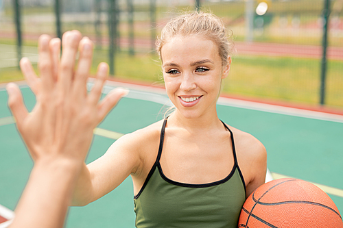 Happy girl with toothy smile making high-five gesture with her friend before or after game of basketball