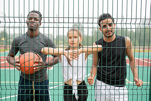 Young active woman and two men in sportswear standing by basketball net in front of camera while having break between games
