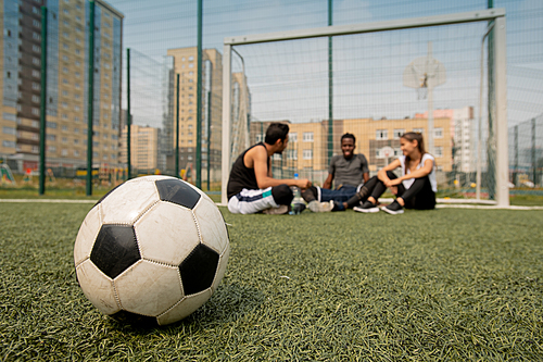 Soccer ball lying on the field or playground on background of three young players having break after training