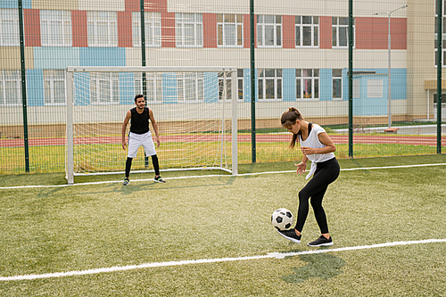 Young female in sportswear standing on soccer field while learning to play with sportsman on background