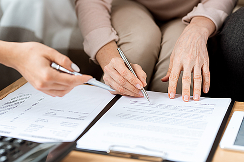 Hands of mature client and real estate agent with pens pointing at contract before signing it