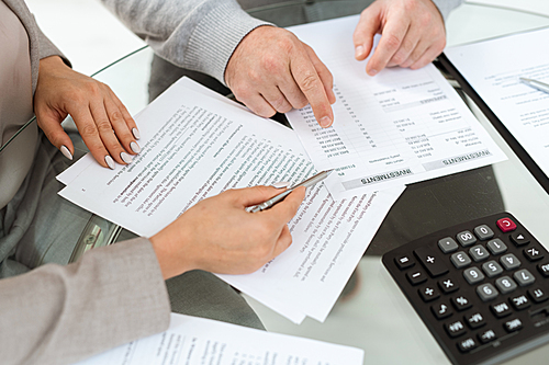 Hands of agent and mature man pointing at financial documents while discussing investments information